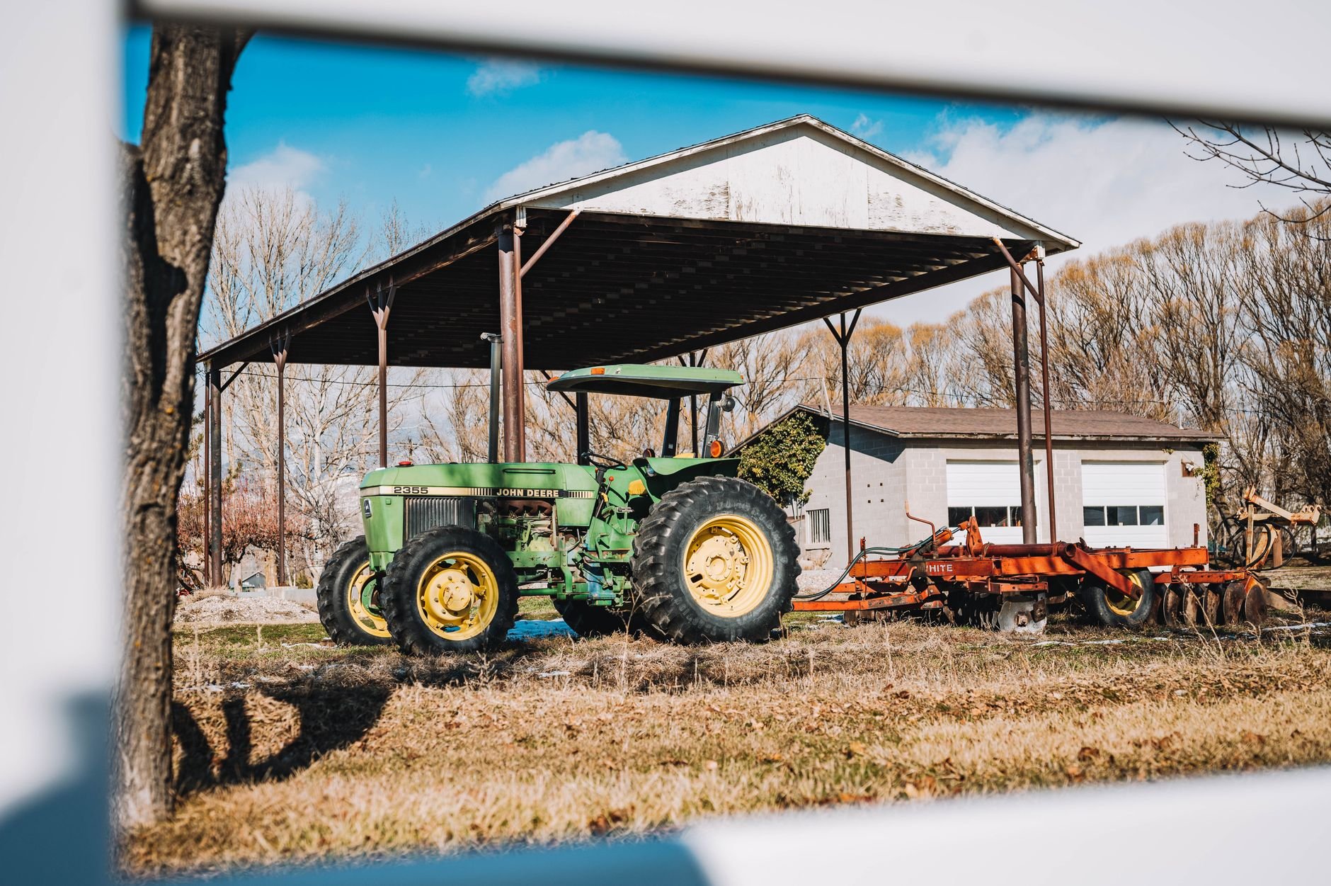 A green tractor parked under a shed on a sunny farm day.